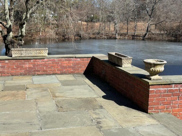 Stone patio with red brick wall, featuring a set of 3 Vintage Rectangular Concrete Planters, and offering views of a frozen pond surrounded by bare winter trees.
