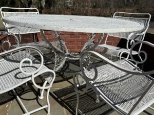 The Vintage White Wrought Iron Outdoor Dining and Conversation Set features intricate designs, perfect on a stone surface with a brick wall backdrop.