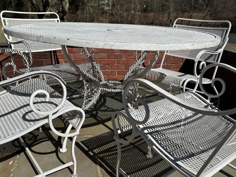 The Vintage White Wrought Iron Outdoor Dining and Conversation Set features intricate designs, perfect on a stone surface with a brick wall backdrop.
