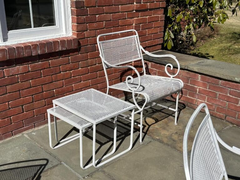 The Vintage White Wrought Iron Outdoor Dining and Conversation Set sits on a sunlit brick patio beside a grassy lawn.