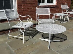 A Vintage White Wrought Iron Outdoor Dining and Conversation Set on a stone patio, placed against a red brick wall.