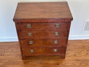 Bachelor's Chest of Drawers featuring four brass handles rests on a hardwood floor.