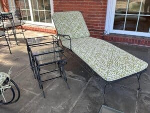 Stone-floored patio featuring a Vintage Wrought Iron Patio Set with green patterned newly upholstered cushioned chaise and nested glass-top tables.