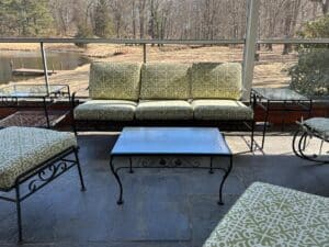 A Vintage Wrought Iron Patio Set with newly upholstered green patterned cushions sits on a screened porch, overlooking a pond and trees.