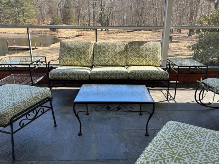 A Vintage Wrought Iron Patio Set with newly upholstered green patterned cushions sits on a screened porch, overlooking a pond and trees.