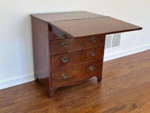 A Bachelor's Chest of Drawers with four drawers and a foldable side extension on a hardwood floor.