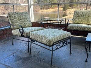 On a tile floor overlooking a pond, the Vintage Wrought Iron Patio Set features newly upholstered green patterned cushions on chairs and a footrest.