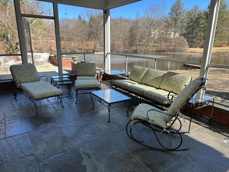 Screened porch featuring a Vintage Wrought Iron Patio Set with Newly Upholstered Cushions, overlooking a pond and trees.