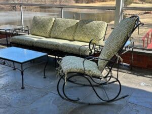 Vintage Wrought Iron Patio Set with newly upholstered green patterned cushions, featuring a sofa, rocking chair, and glass-topped table near a lake.