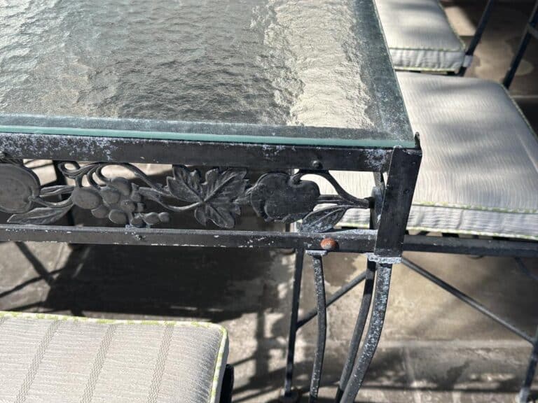 A Vintage Wrought Iron Grapevine Dining Set with a decorative glass-top table is surrounded by cushioned chairs.
