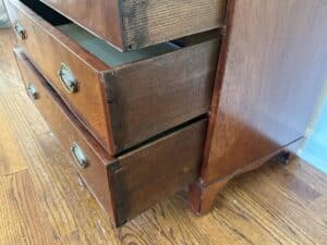 The Bachelor's Chest of Drawers, featuring two drawers slightly open with circular handles, sits on a wooden floor.