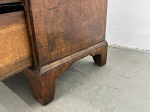 A partially open, ornate carved drawer from the Antique Burl Chest of Drawers sits prominently on a gray concrete floor.