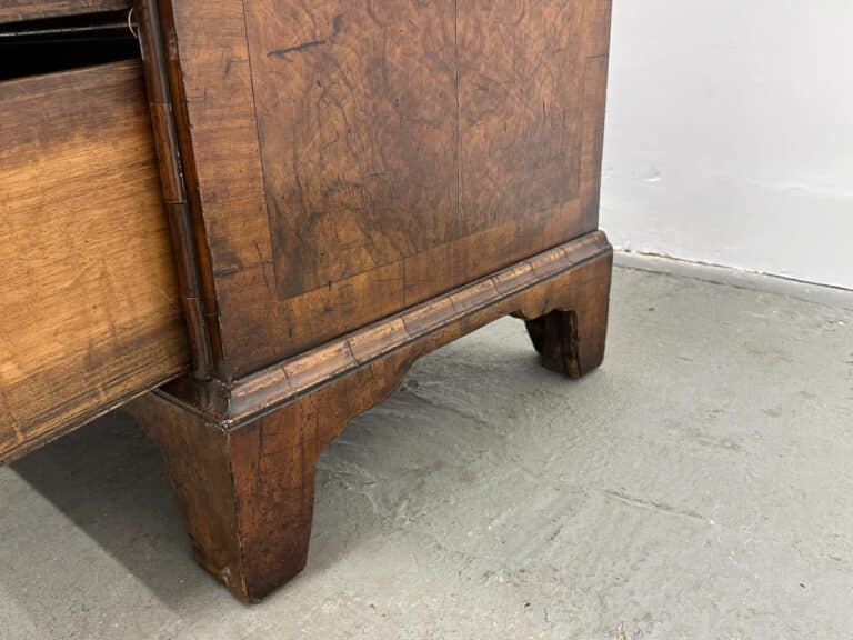 A partially open, ornate carved drawer from the Antique Burl Chest of Drawers sits prominently on a gray concrete floor.