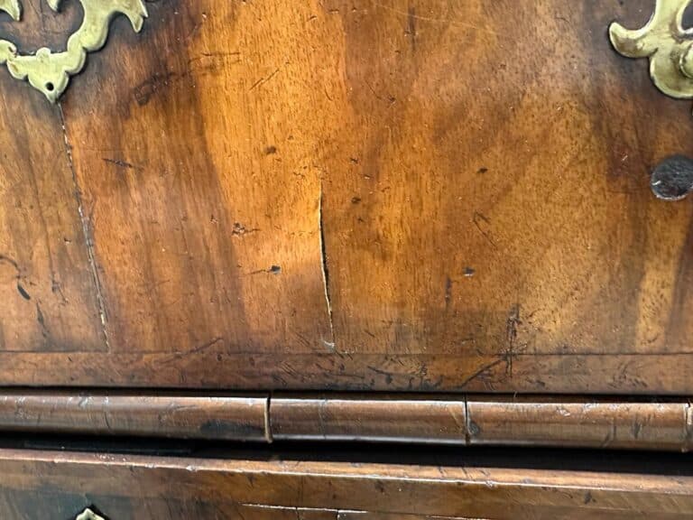 Close-up of the Antique Burl Chest of Drawers, highlighting a wooden surface with a visible crack and ornate metal corner detailing.