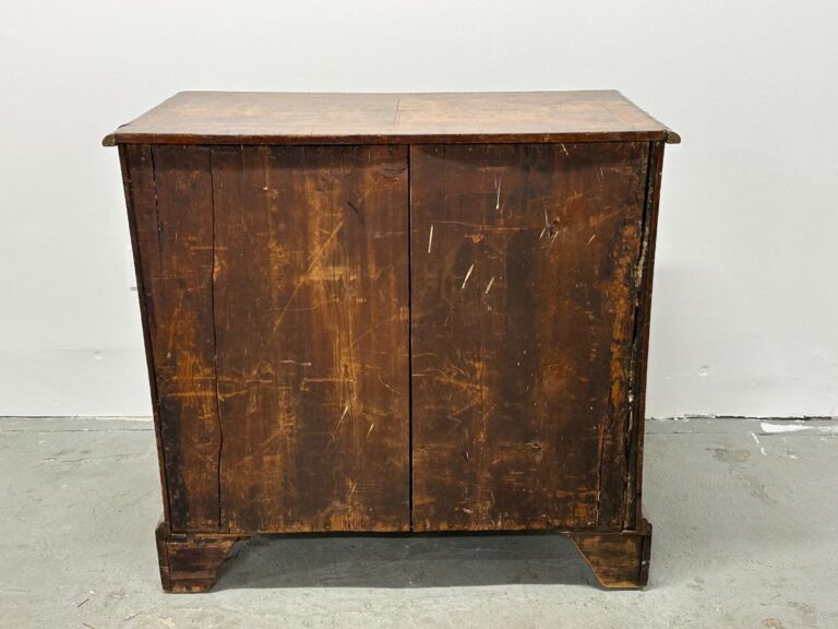 An Antique Burl Chest of Drawers with a weathered appearance and a scratched surface stands against a plain white wall.