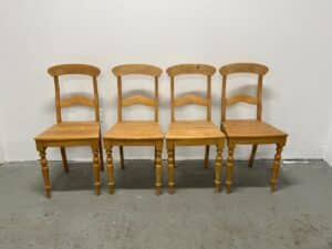 Four wooden chairs with curved backs and carved legs against a plain white wall.