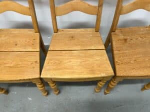 Three wooden chairs with ladder backs, one chair in the middle has a broken seat.
