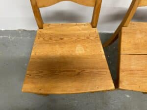 Wooden chair with a flat seat and a simple curved backrest on a gray concrete floor.