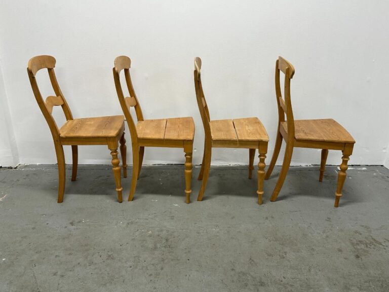 Four wooden chairs with rounded backs are placed in a line on a concrete floor against a white wall.