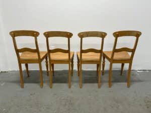 Four wooden chairs lined up against a white wall, viewed from the back.