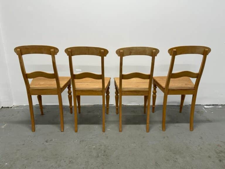 Four wooden chairs lined up against a white wall, viewed from the back.