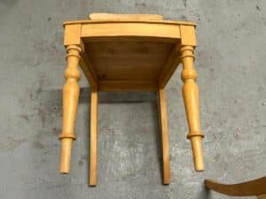 Wooden table with one corner resting on the ground, showing two ornate legs and two missing legs.