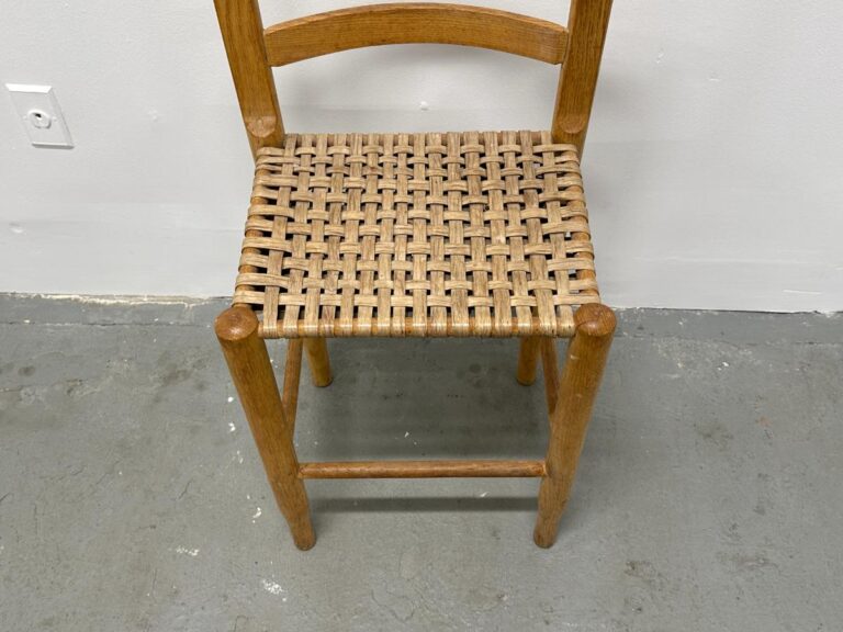 Wooden chair with a woven seat, placed on a gray concrete floor near a white wall socket.