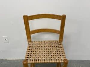Wooden chair with a woven seat against a plain white wall.