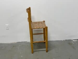 A wooden chair with a woven seat and backrest standing against a plain white wall.