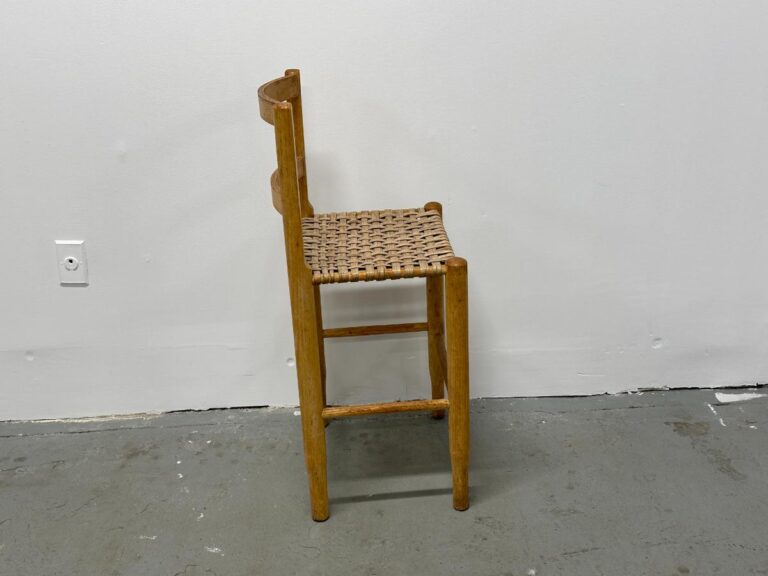 A wooden chair with a woven seat and backrest standing against a plain white wall.