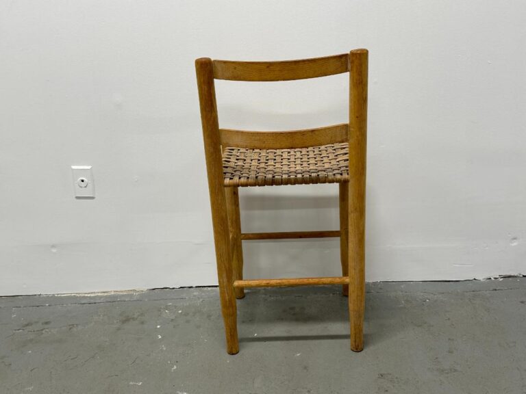 Wooden chair with a woven seat against a white wall and gray floor.