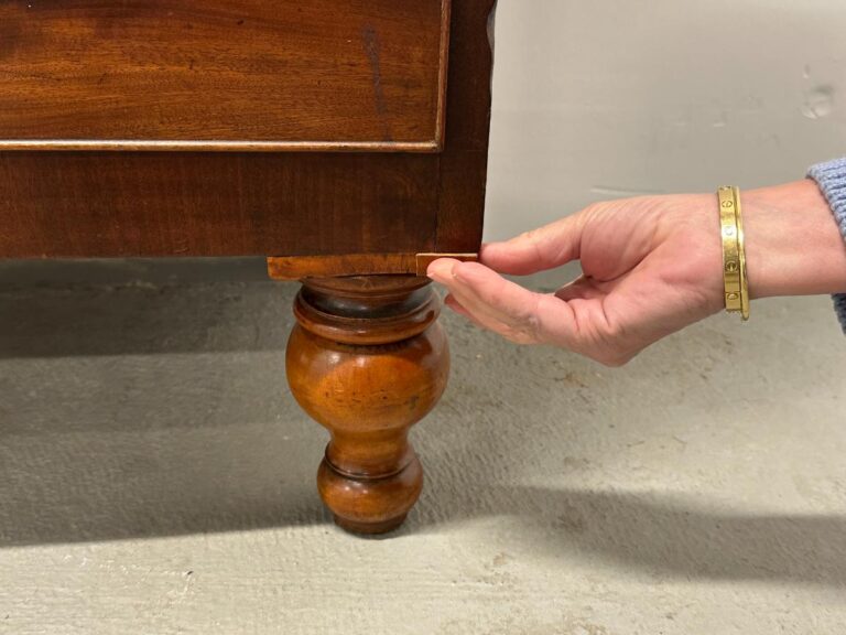 Hand touching corner of wooden furniture leg with decorative design on concrete floor.