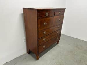 Vintage wooden dresser with six drawers and metal handles in a white, minimalistic room.