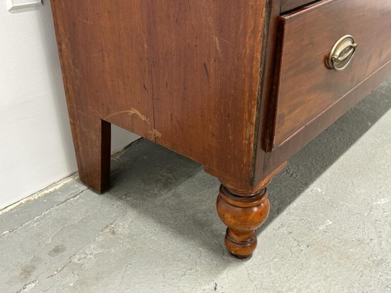 Close-up of a wooden dresser corner with a carved leg on a gray concrete floor.