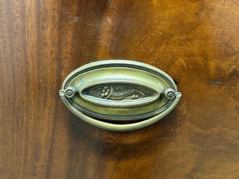 Ornate brass drawer handle on a wooden surface with a carved floral design.