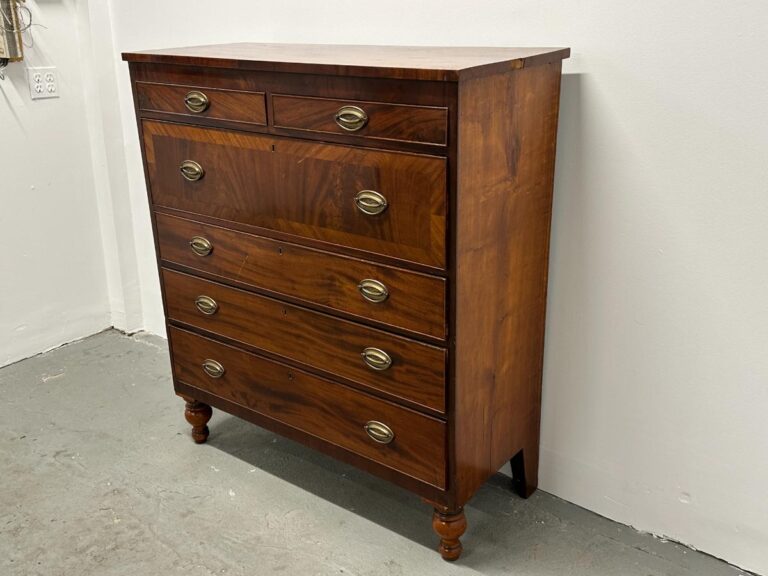 A vintage wooden dresser with five drawers and brass handles against a plain white wall.