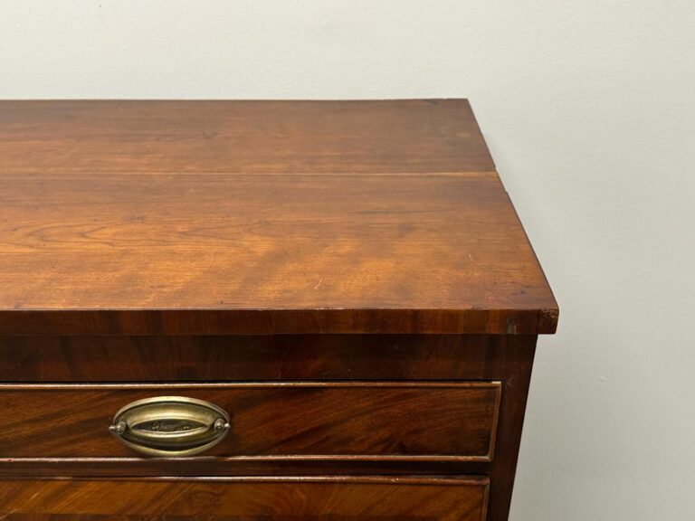 Close-up of a wooden dresser corner with brass handle against a plain white wall.