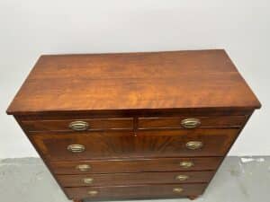 Wooden chest of drawers with brass handles, against a plain white wall.