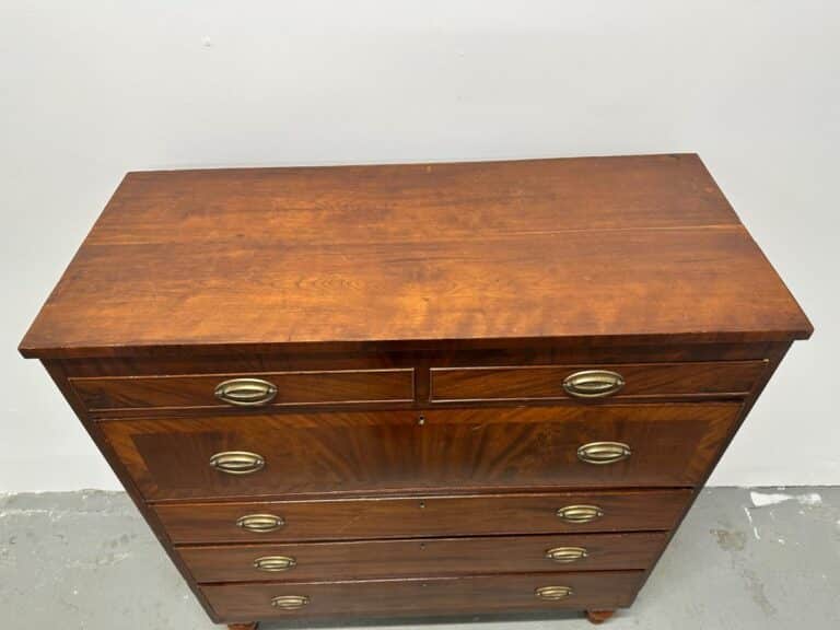 Wooden chest of drawers with brass handles, against a plain white wall.