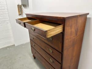 Wooden dresser with six drawers, two on top slightly open, against a white and gray wall.