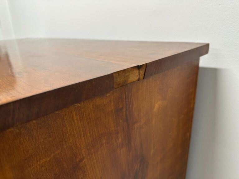 Damaged corner of a wooden cabinet against a white wall.