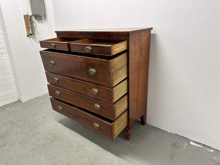 Wooden dresser with five drawers, upper two drawers open, against a white wall on a gray floor.