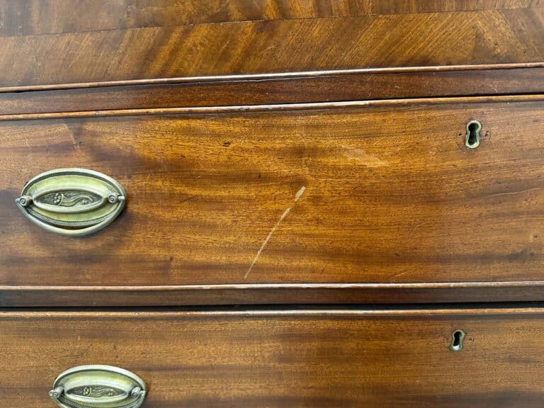 Close-up of a wooden dresser with brass handles and keyholes, featuring a prominent scratch in the wood.