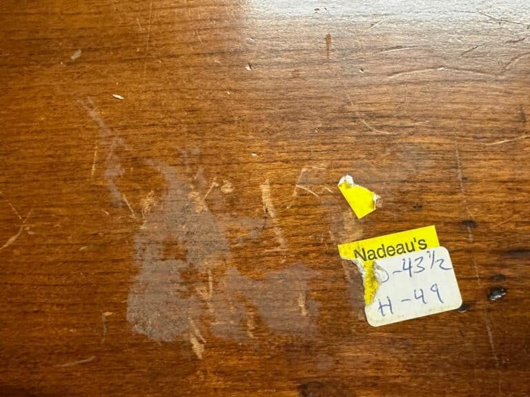 Wooden surface with faded marks and a worn yellow label reading "Nadeau's," alongside other numbers and smudges.