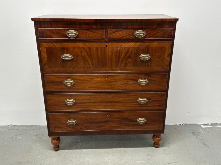 A vintage wooden chest of drawers with five drawers and metal handles, standing on short legs against a white wall.