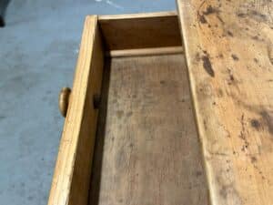 Open empty wooden desk drawer with a round knob, showing a worn surface and some scratches.