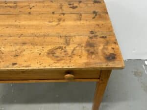 Wooden table with visible stains and a small drawer, set against a gray floor and white wall.