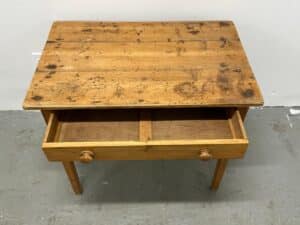 Wooden table with two open drawers, each with round knobs, against a plain white wall.