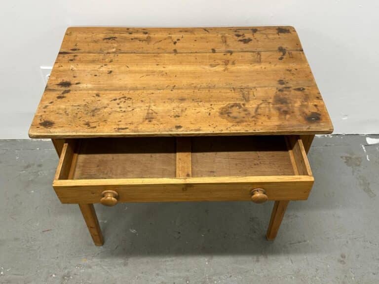 Wooden table with two open drawers, each with round knobs, against a plain white wall.