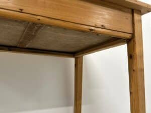 Wooden table with a rustic finish, viewed from below against a white wall background.